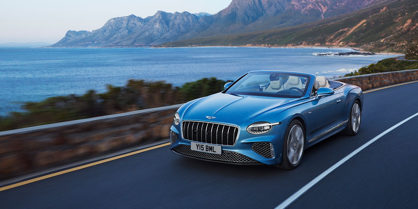 Bentley Milano New Bentley Continental GTC Azure convertible in Light Windsor blue paint with 22 inch Azure wheels and chrome grill, driving dynamically by the sea