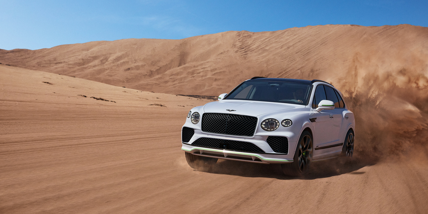 Bentley Milano Bentley Bentayga Speed SUV front three quarter in Snow Quarts Pearlescent by Mulliner white paint driving dynamically through the desert