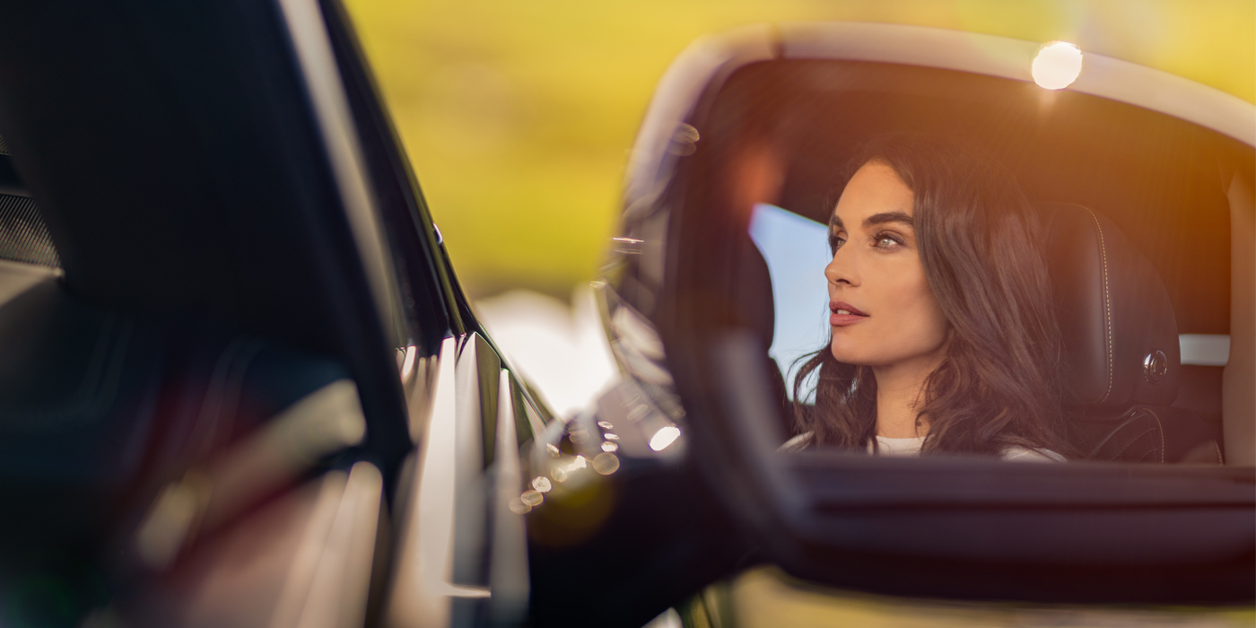 Bentley Milano profile of dark haired woman's face in mirror of Bentley car in sunlight