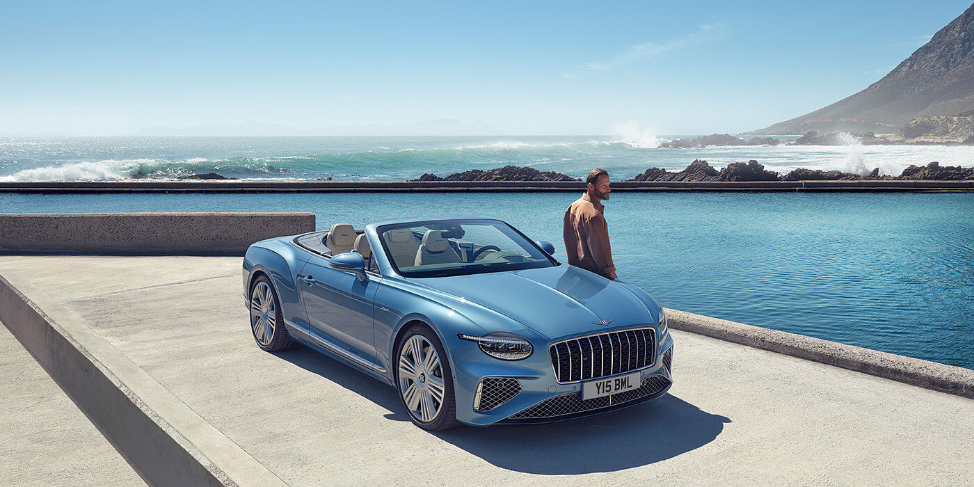 Bentley Milano New Bentley Continental GTC Azure convertible front view in Light Windsor blue paint with 22 inch ten spoke wheels parked by the sea in the sunshine