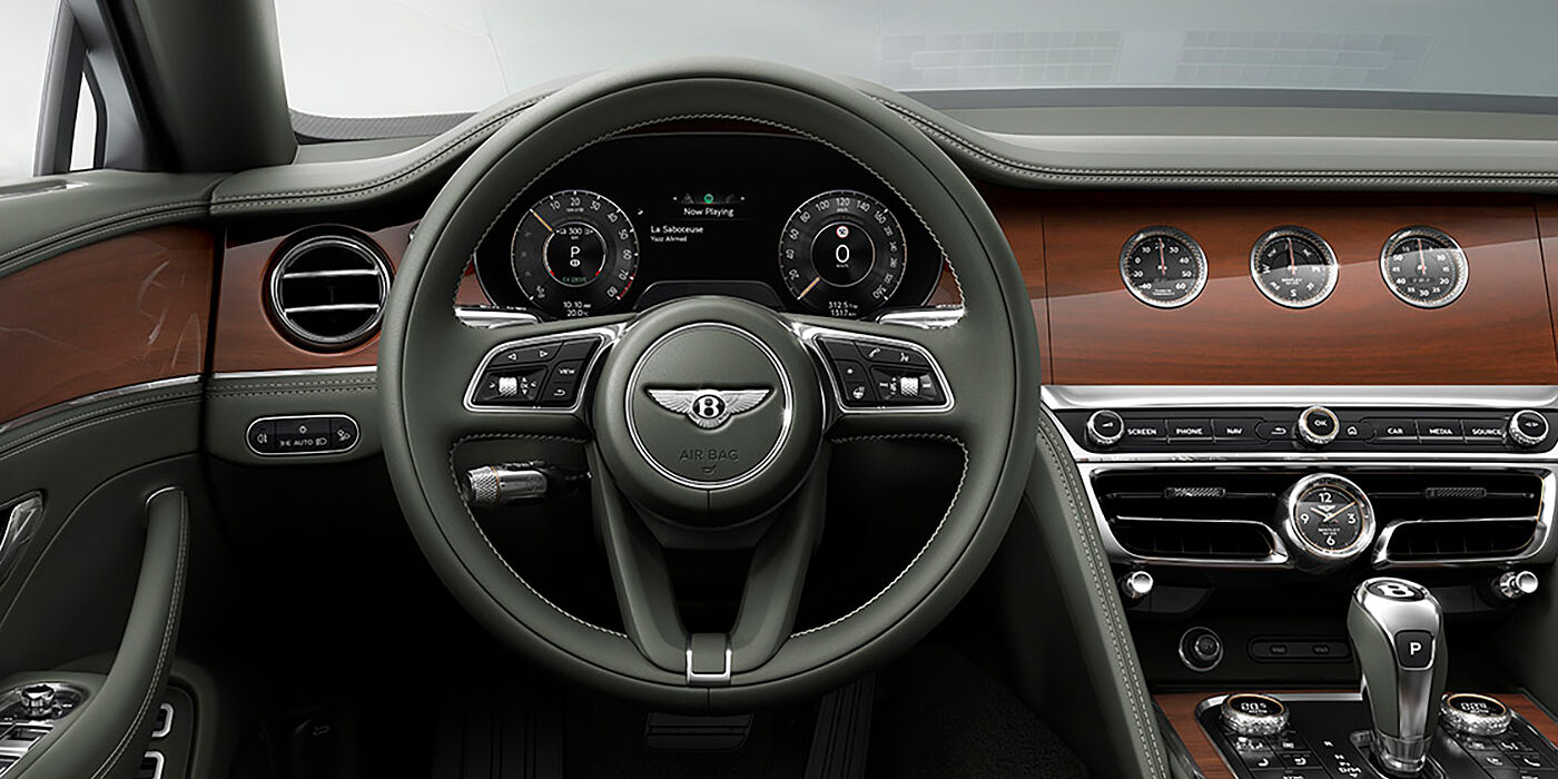 Bentley Milano New Bentley Flying Spur sedan front cabin in Cumbrian Green hide and Crown Cut walnut veneer showing steering wheel and Rotating Display with three clocks on face
