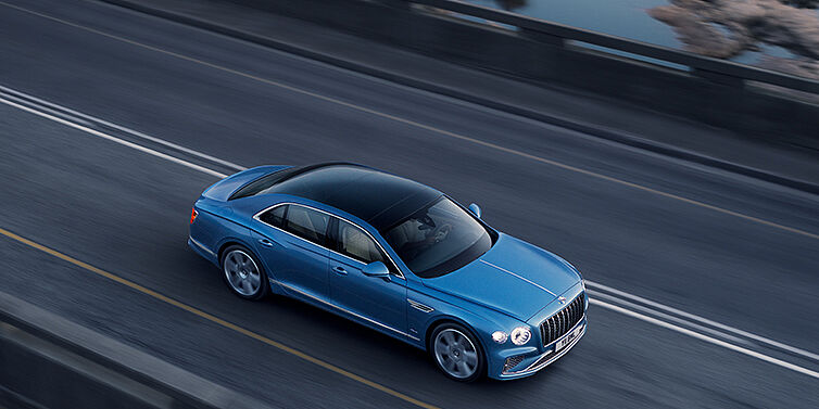 Bentley Milano New Bentley Flying Spur Azure sedan in Light windsor blue paint by Mulliner, with 22 inch Azure wheels seen from overhead driving dynamically on a country road